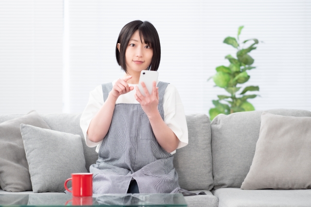 ソファに座り休憩しながらスマートフォンを操作する女性介護スタッフ