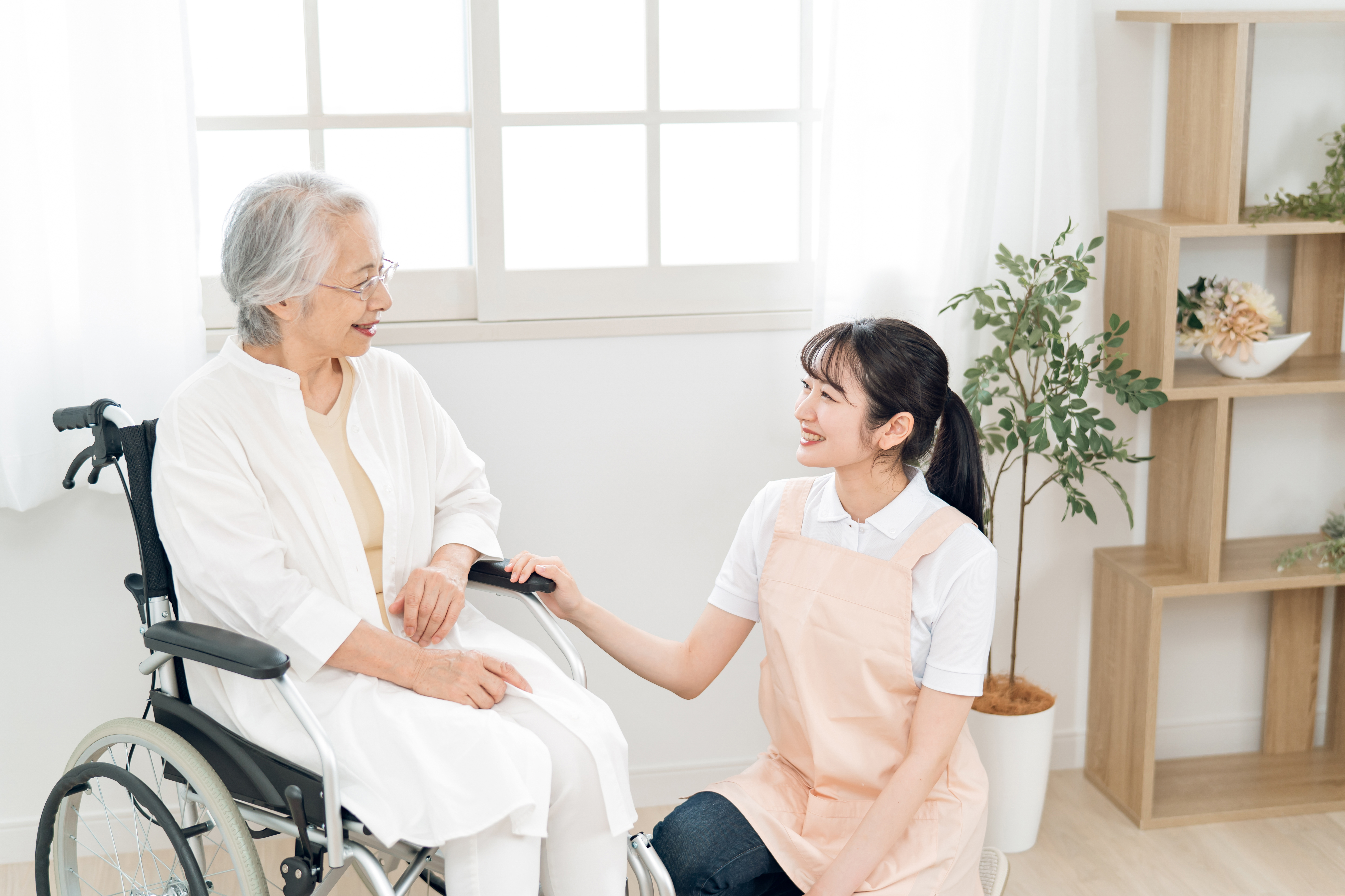 車椅子に乗った高齢女性と介護スタッフが会話している様子