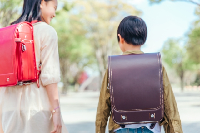 赤いランドセルを背負った高学年ぐらいの女の子と茶色いランドセルの中学年ぐらいの男の子の後ろ姿