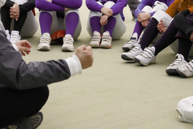 指導者を囲んで座っているスポーツ選手達