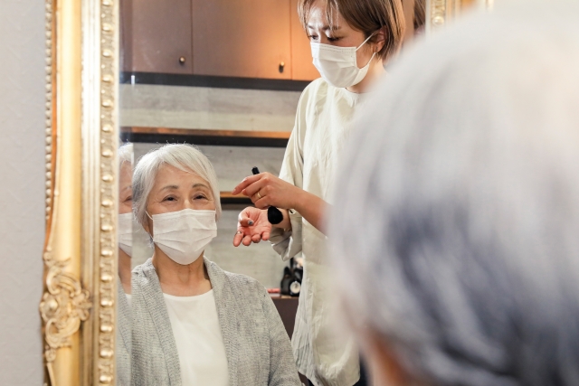 女性にメイクをしてもらっている笑顔の高齢女性