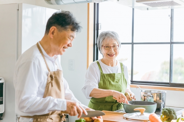 笑顔で会話しながら台所で調理をおこなう高齢の男女